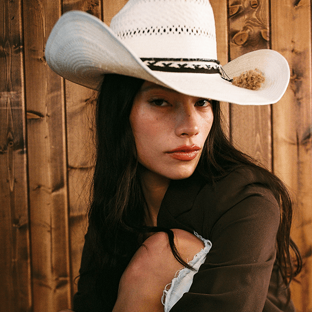 Woman wearing a white cowboy hat against a wooden background
