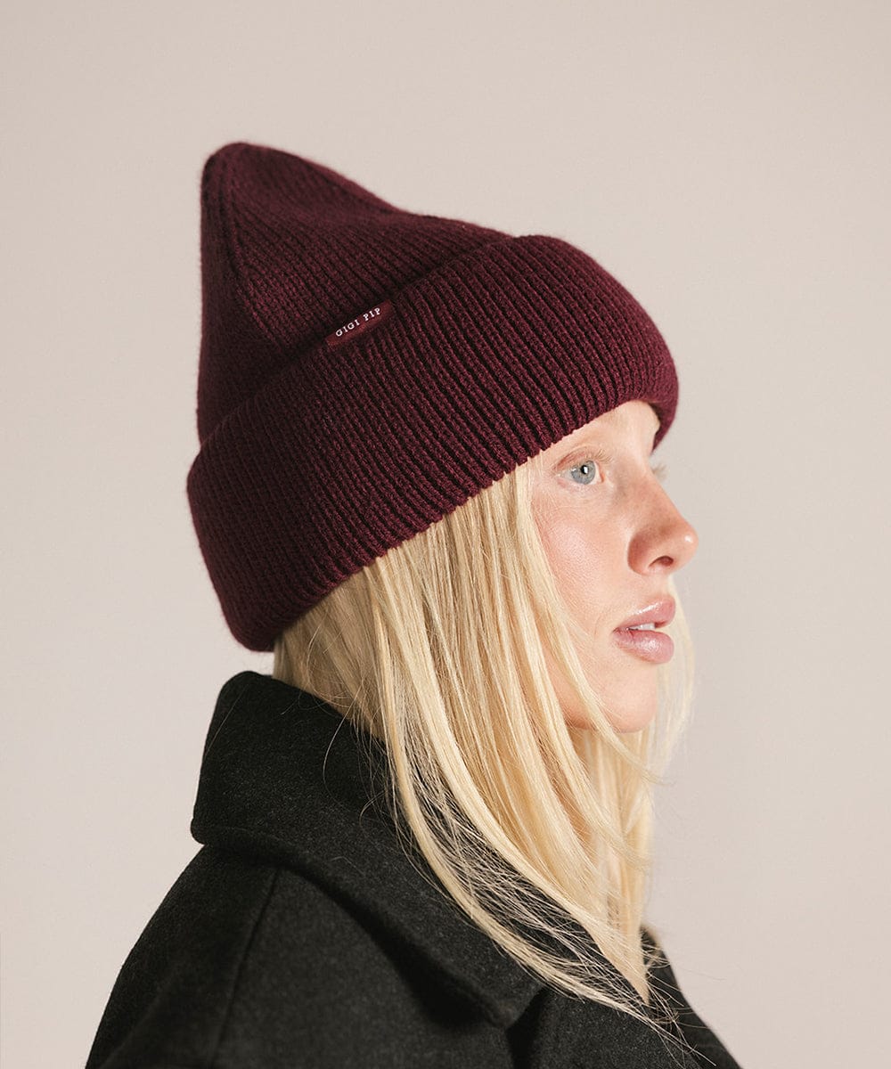 Person wearing a maroon beanie and dark coat against a beige background #color_merlot