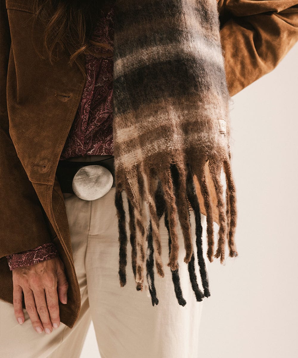 Person wearing a plaid scarf with fringe, brown coat, and beige pants on a neutral background #color_Brown - Black Plaid