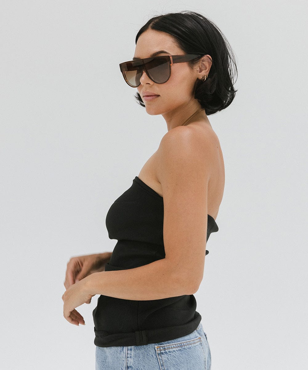 Woman wearing amber colored sunglasses, a black top and blue jeans, posing against a plain background #color_amber
