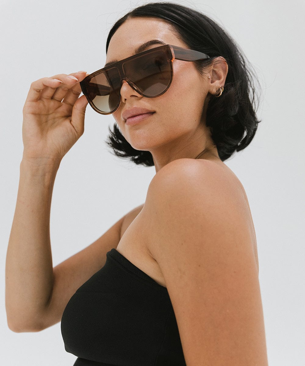 Woman wearing amber colored sunglasses and a black top, looking sideways against a plain background #color_amber