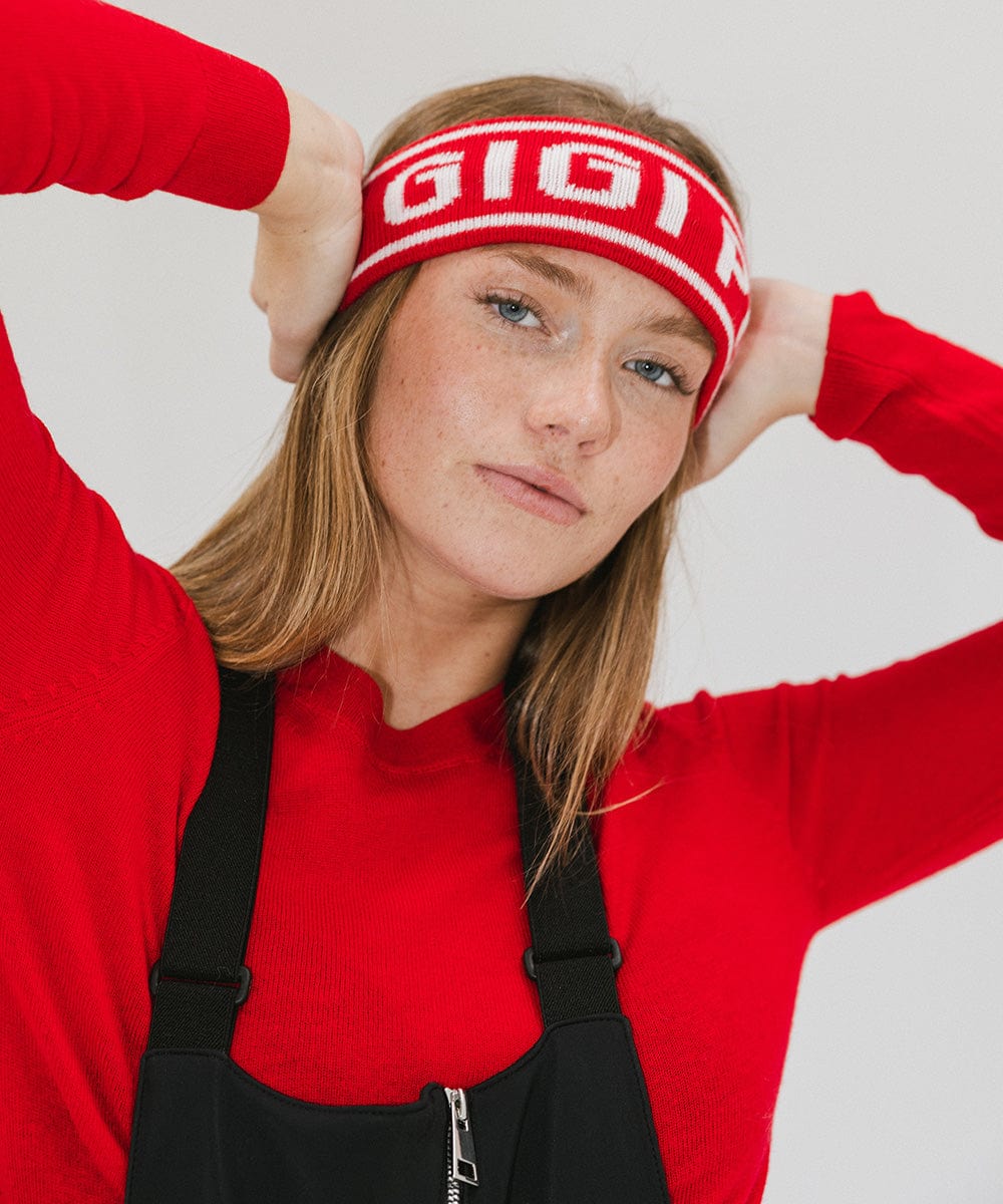 Woman wearing a ruby red colored headband with 'GIGI PIP' text and a red t-shirt with a black sleeveless jacket against a plain background #color_ruby red