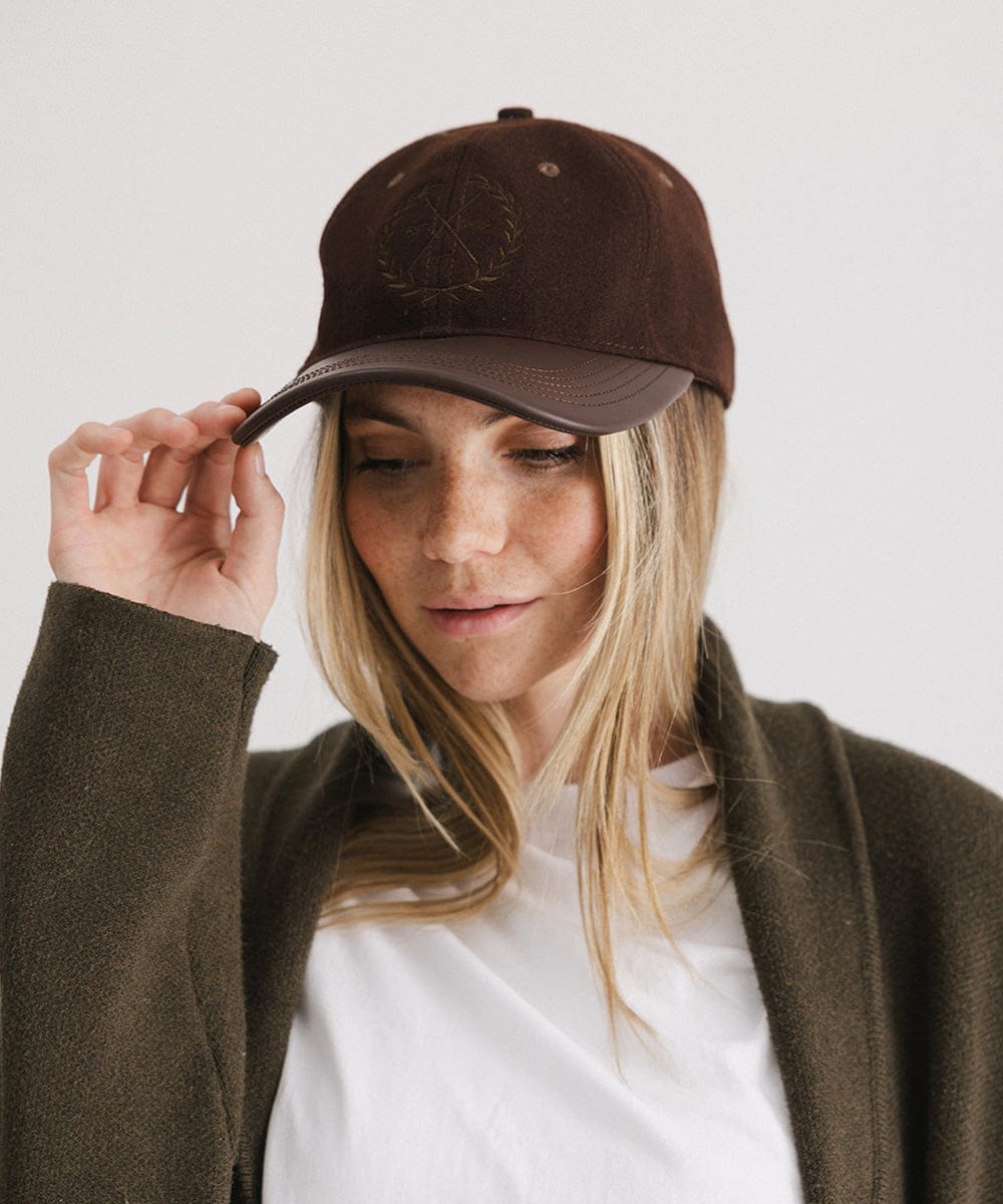 Woman wearing a brown cap with a logo and a white t-shirt with a brown coat, posing against a plain background #color_brown