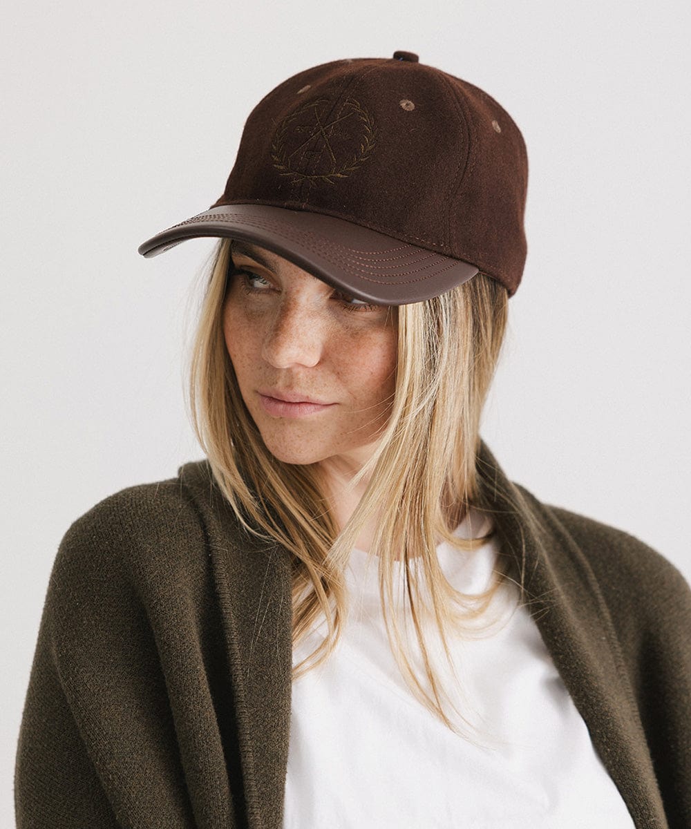 Woman wearing a brown cap with a logo and a white t-shirt with a brown coat, looking sideways against a plain background #color_brown