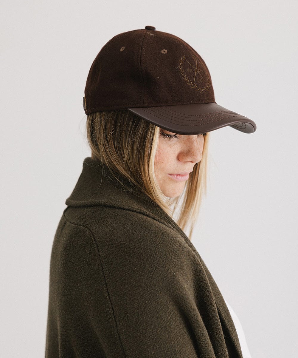 Woman wearing a brown cap with a logo and a white t-shirt with a brown coat, facing sideways against a plain background #color_brown
