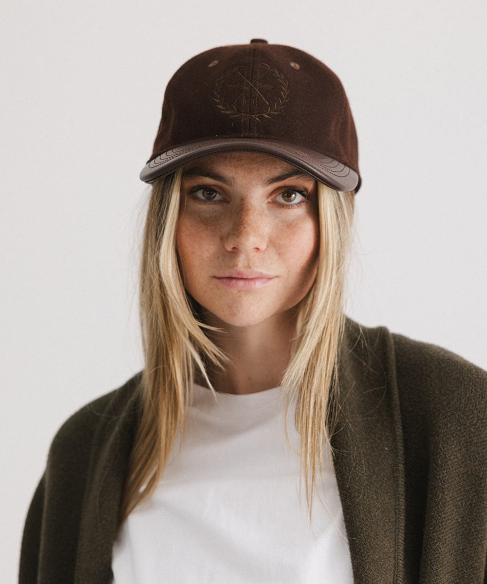 Woman wearing a brown cap with a logo and a white t-shirt with a brown coat against a plain background #color_brown
