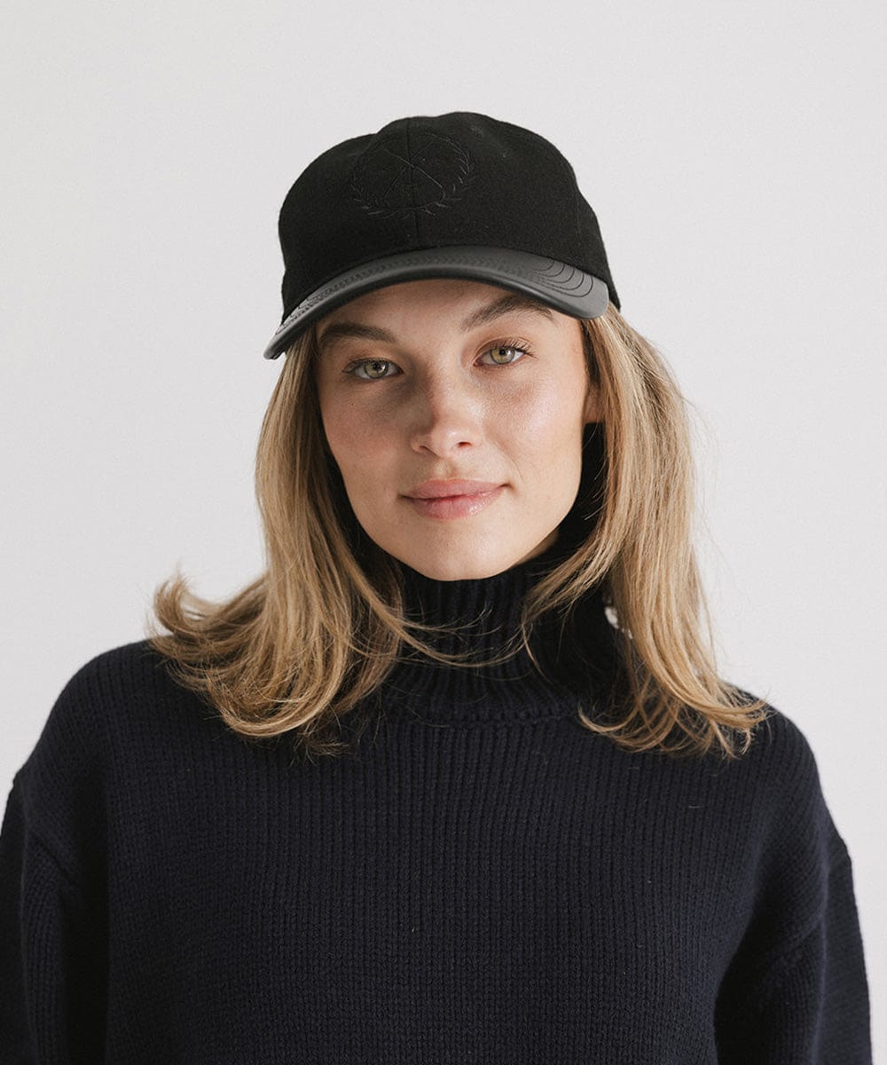 Woman wearing a black cap with a logo and a black sweater against a plain background #color_black
