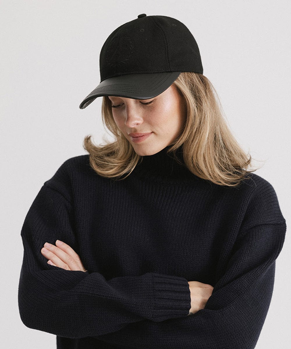 Woman wearing a black cap with a logo and a black sweater, posing against a plain background #color_black