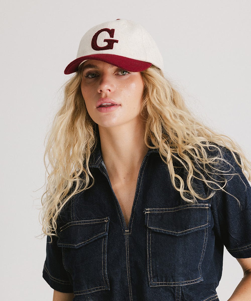 Woman wearing a white and burgundy baseball cap with the letter 'G' and a denim shirt against a plain background #color_burgundy