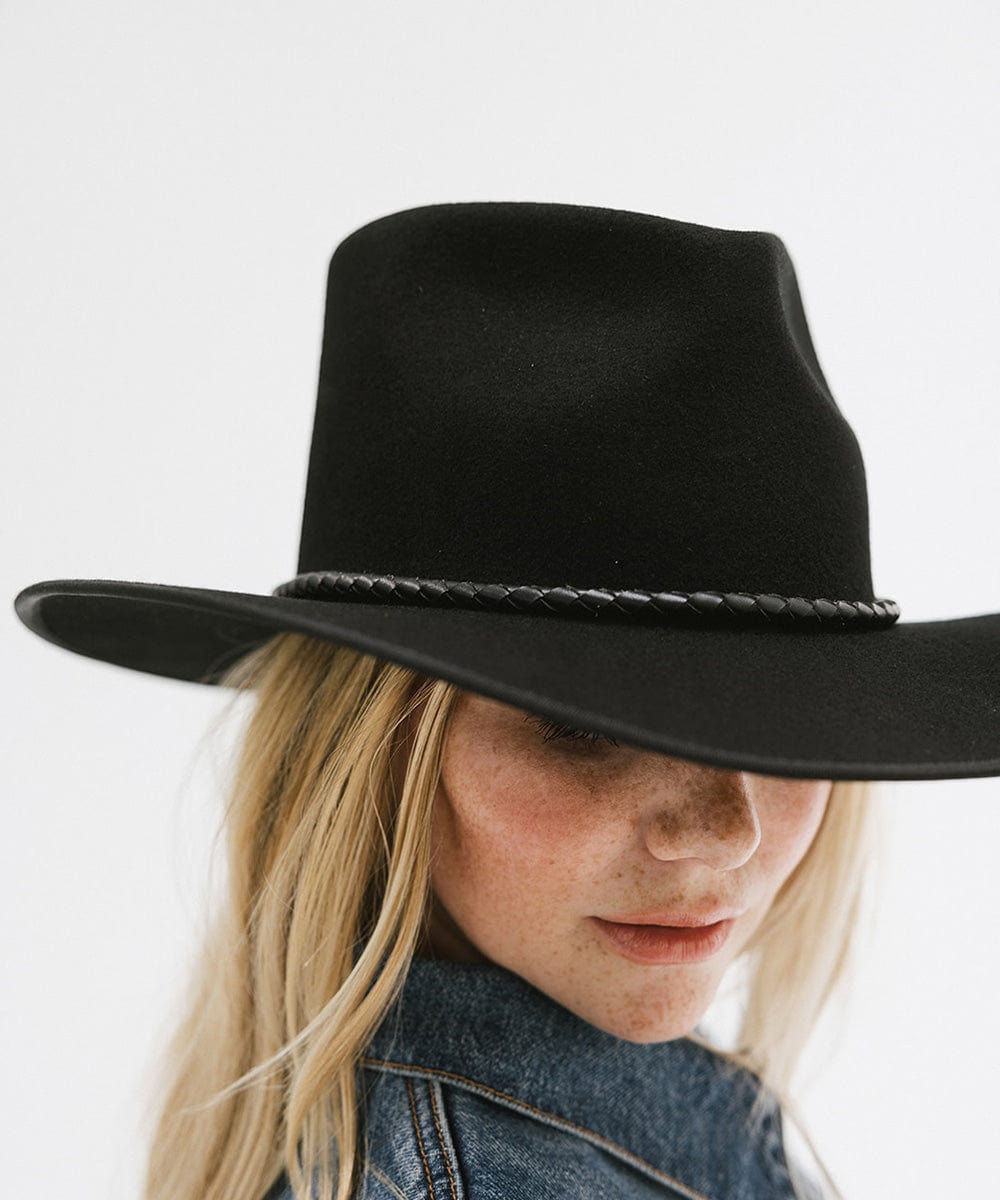 Woman wearing a black hat with a black braided bolo hat band against a plain background #color_black
