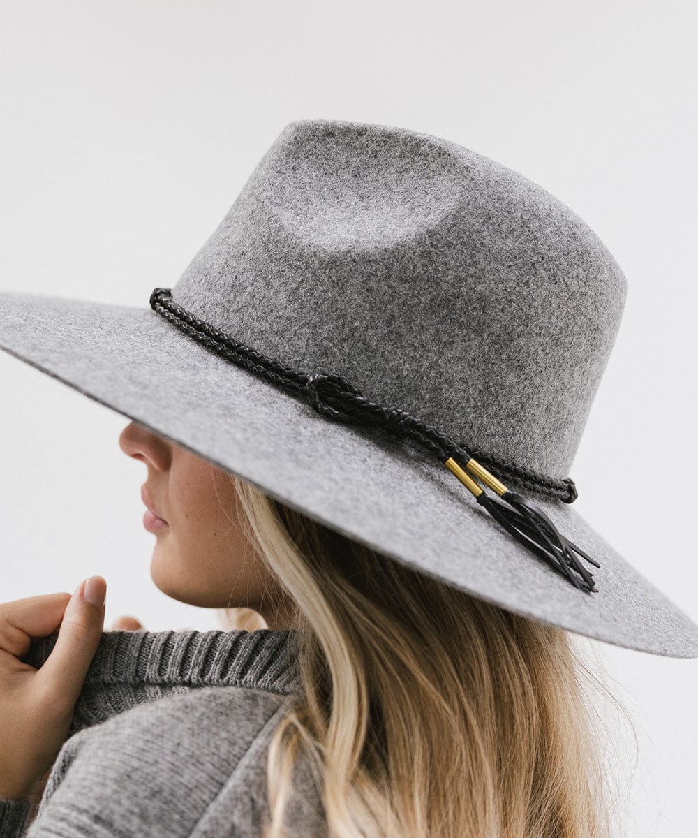 Woman wearing grey cowboy hat with a black lasso braided hat band and a grey sweater, facing sideways against a plain background #color_brown #color_black