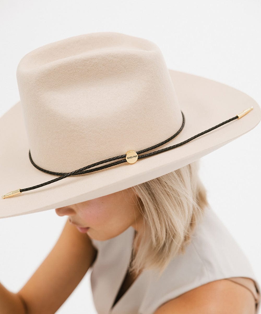 Woman wearing a cream cowboy hat with a black braided hat band and a white top, facing sideways against a plain background #color_black