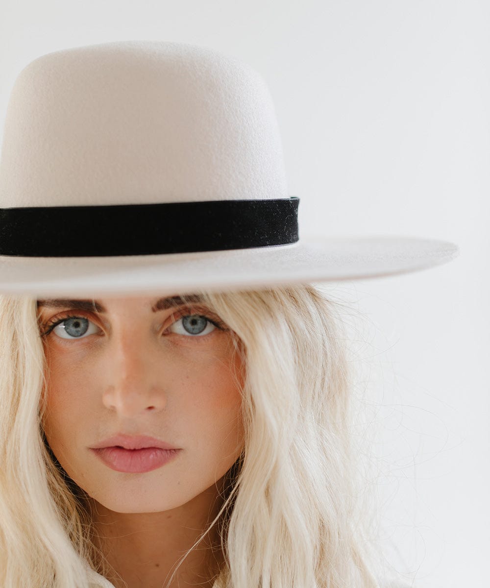 Woman wearing a white hat with a black velvet chain hat band against a plain background #color_black