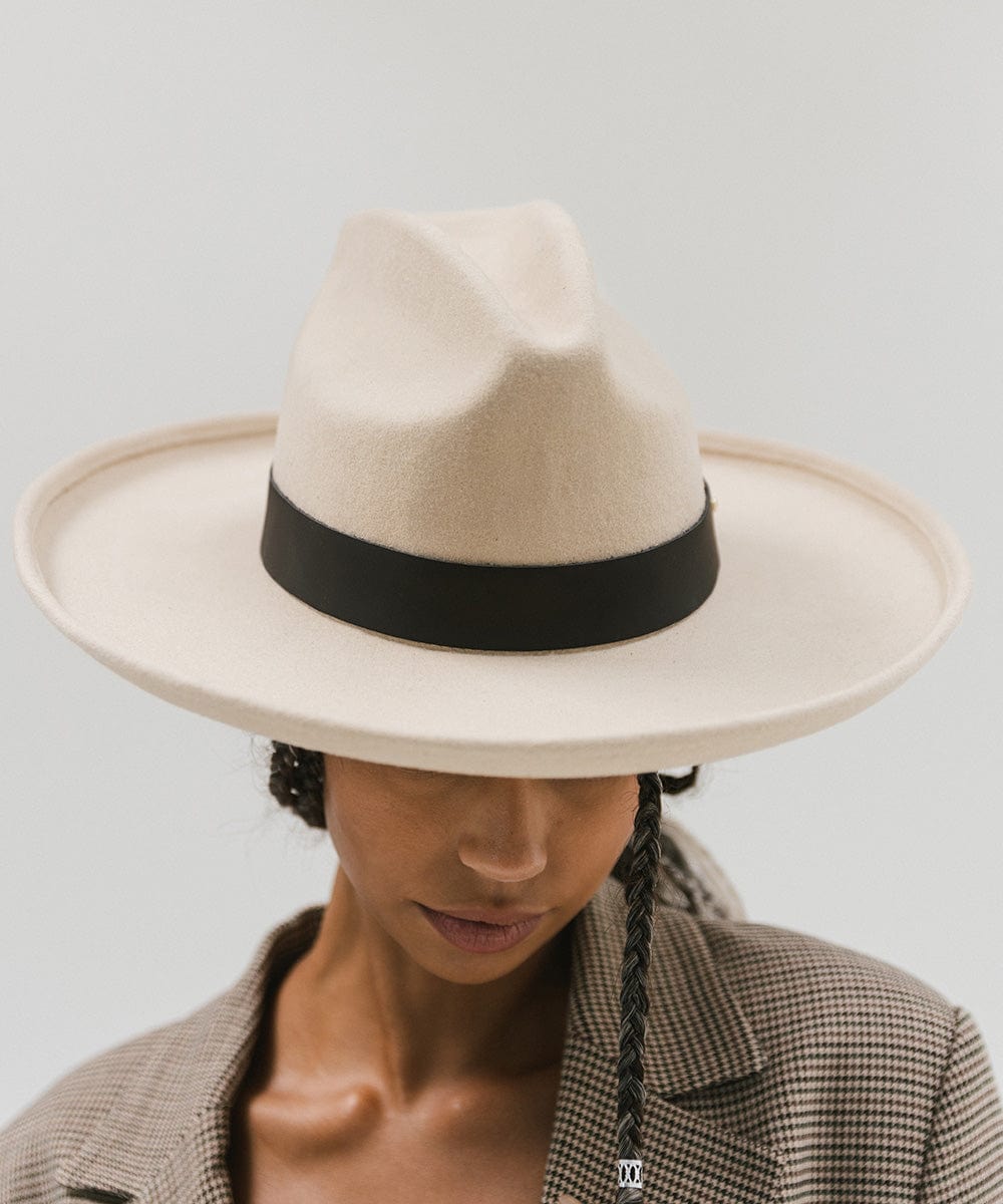 Person wearing a cream hat with a wide black leather band around the base against a plain background #color_black