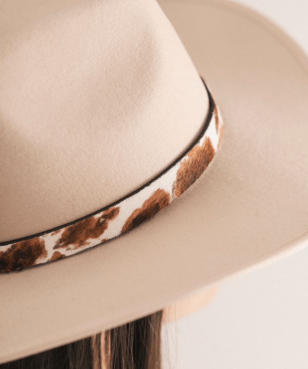 Woman wearing a beige cowboy hat with a cowhide decorative band on a white background #color_brown