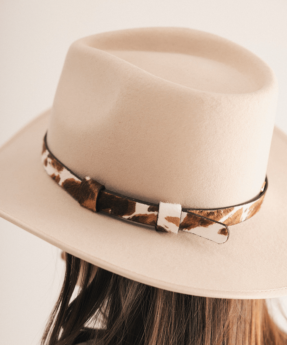 Woman wearing a beige cowboy hat with a cowhide decorative band on a white background #color_brown
