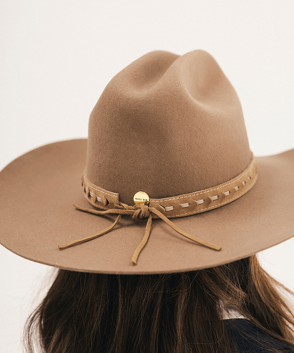 A close-up back view of a person wearing a tan wide-brim felt cowboy hat with a matching leather band, white stitching, and a small gold bell accent #color_camel