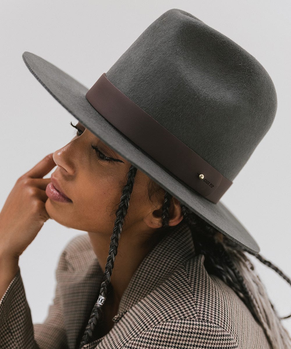 A person wearing a grey hat with a wide chocolate colored leather band around the base, and a coat, posing sideways against a plain background #color_chocolate