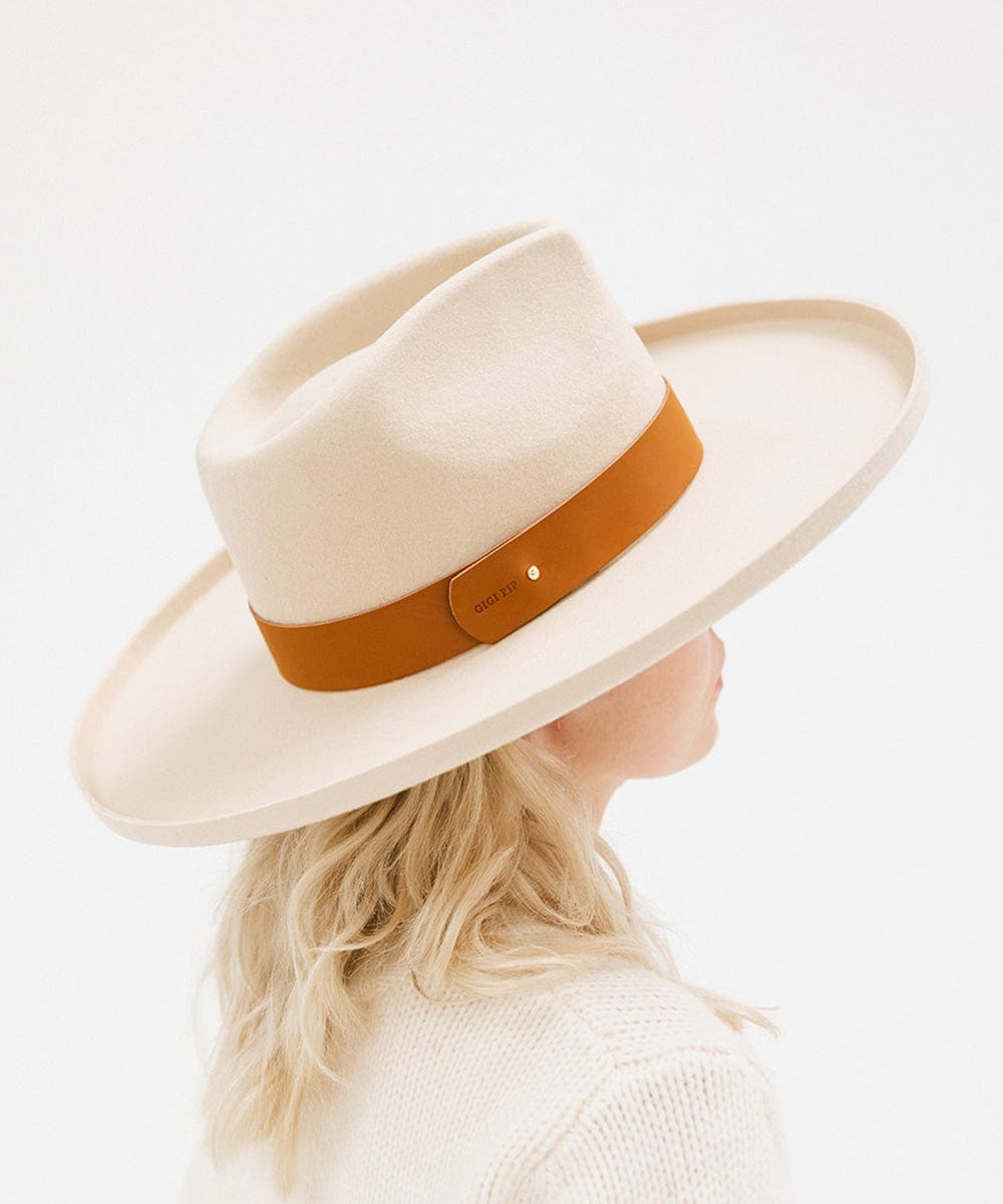 A person wearing a cream hat with a wide cognac leather band around the base, facing sideways against a plain background #color_cognac