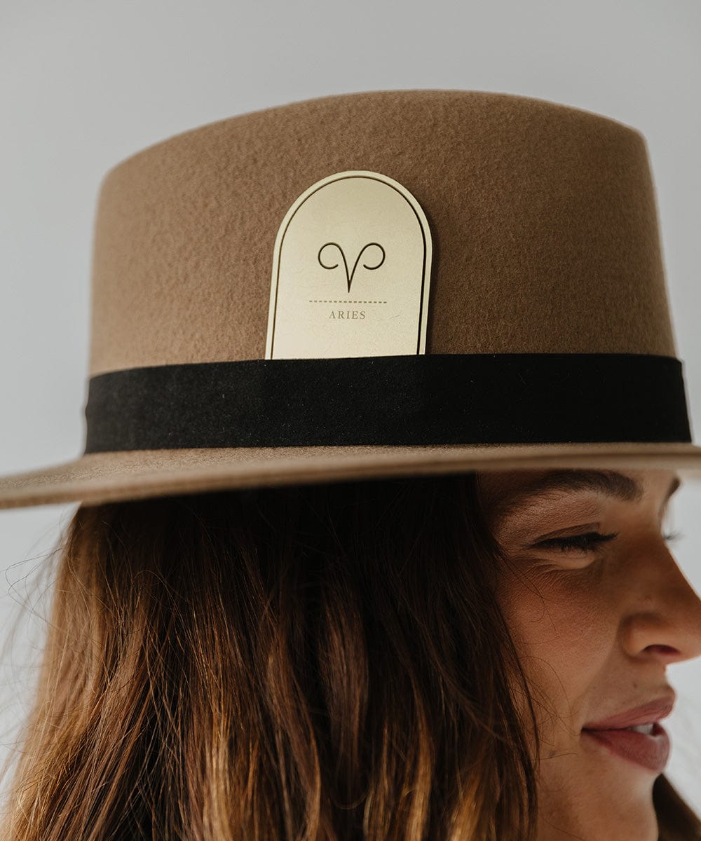 Woman wearing a brown hat with a black band and a gold 'Aries' zodiac band card against a plain background #color_gold