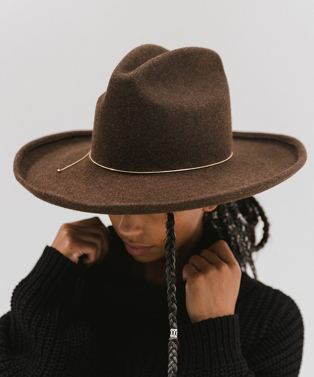 Woman wearing a brown hat with a gold chain bolo hat band and a black sweater, posing against a plain background #color_gold