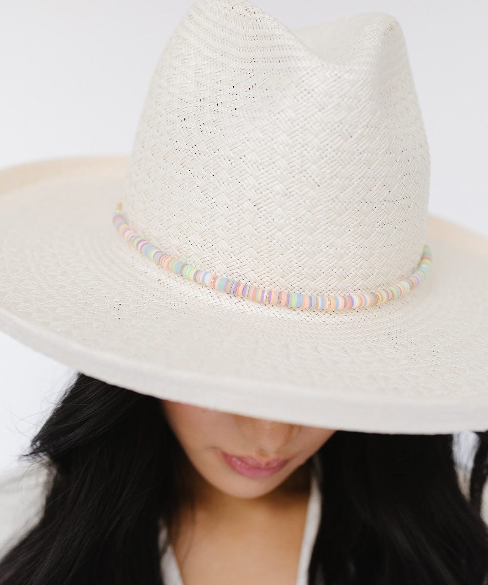Woman wearing a white hat with a multi colored beaded hat band against a plain background #color_multi