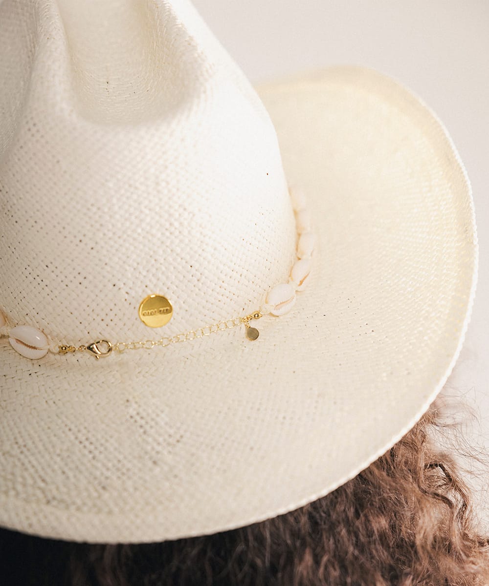 Close-up of a woman wearing a white straw hat with shell embellishments and gold Gigi Pip pin #color_natural