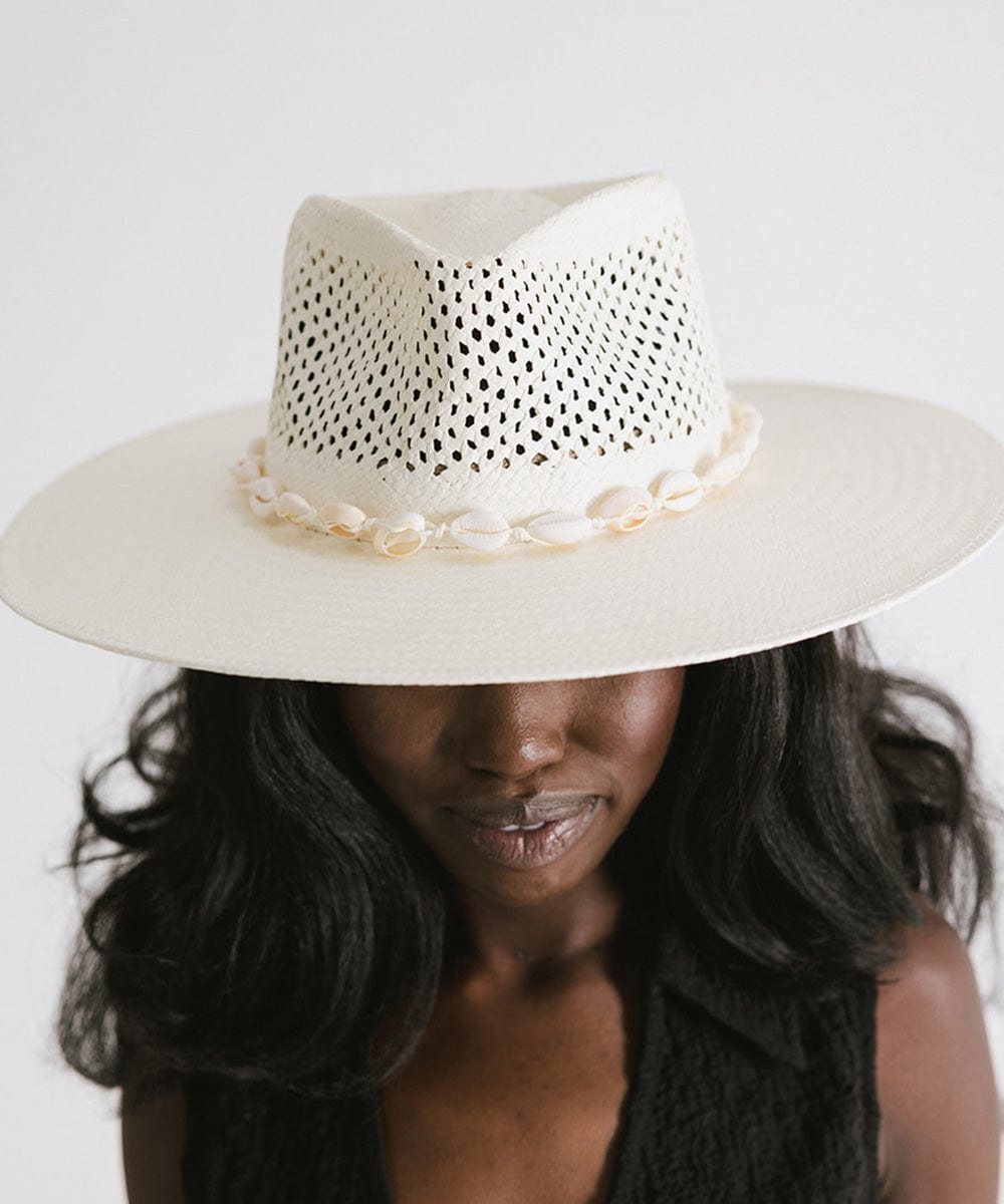 Woman wearing a white hat with a white shell hat band and a black top against a plain background #color_white