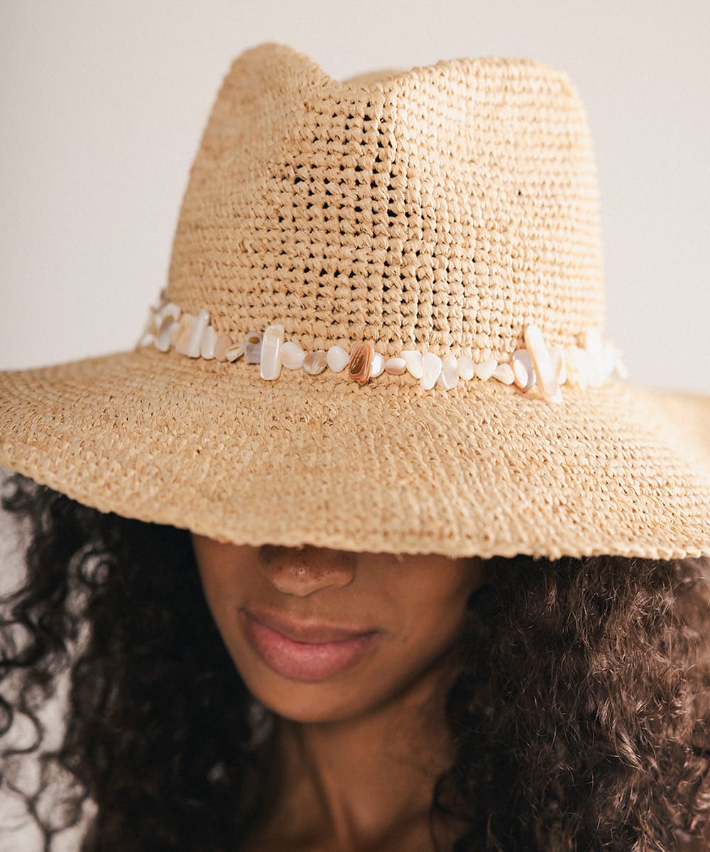 Woman wearing a straw hat with decorative shells on a plain background #color_natural