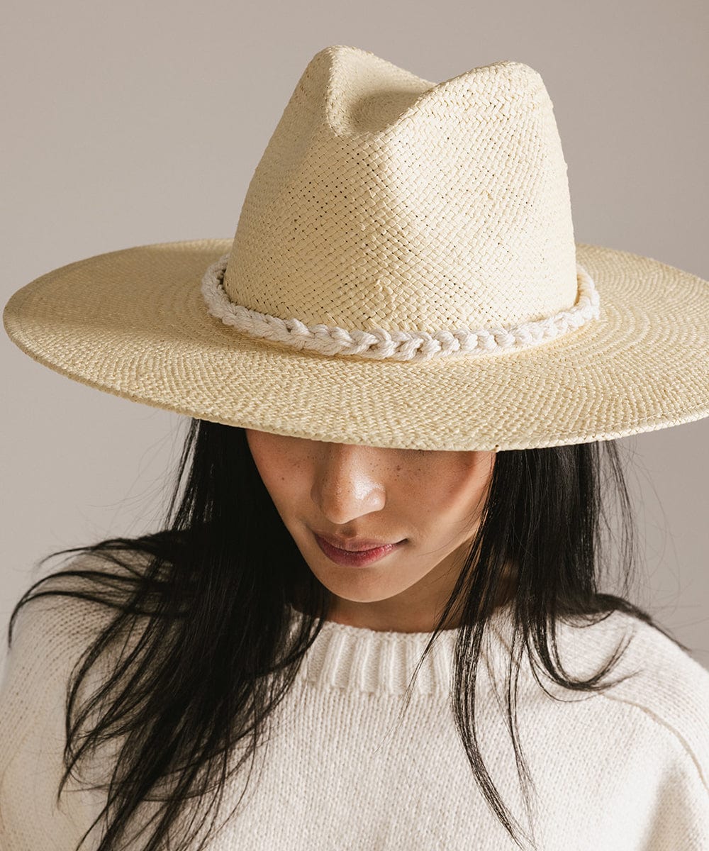 Woman wearing a beige cap with a natural white colored braided rope hat band and a white sweater, looking down against a plain background #color_natural white