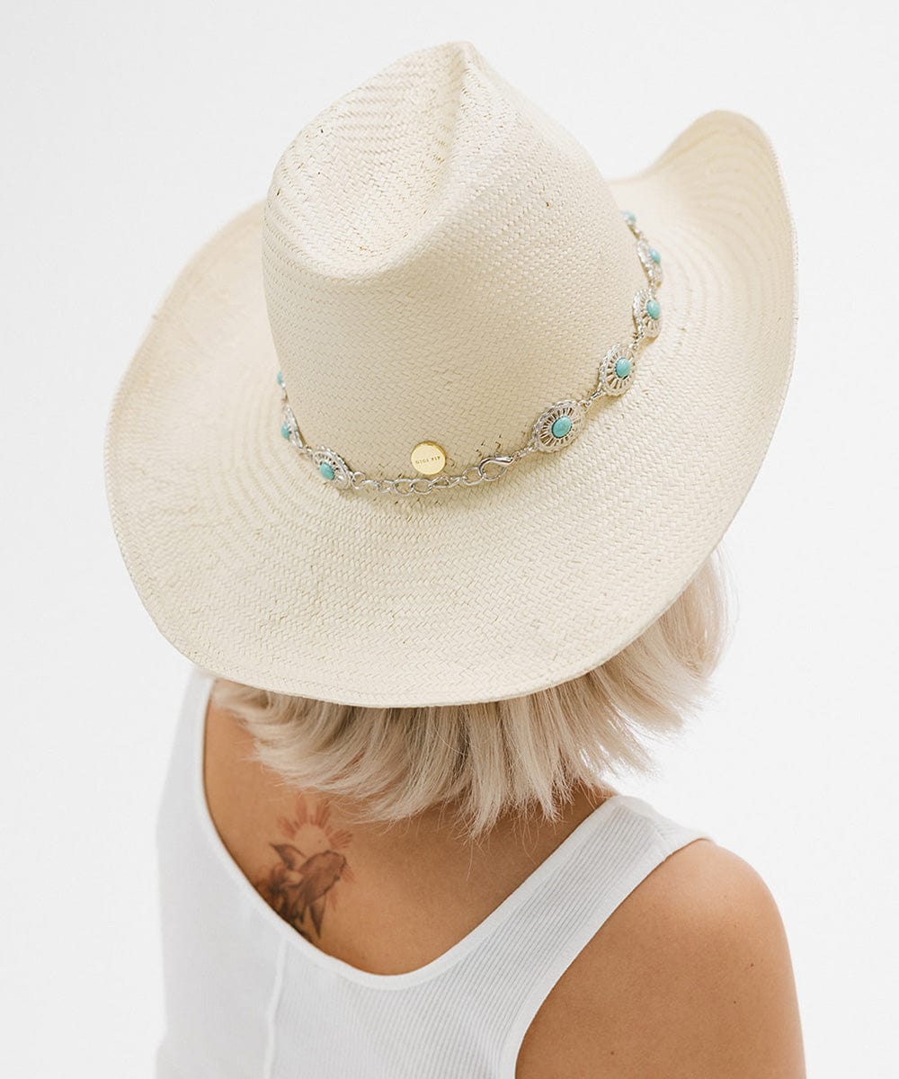 Woman wearing a white cowboy hat with a silver and turquoise concho hat band and a white top, facing behind against a plain background #color_silver
