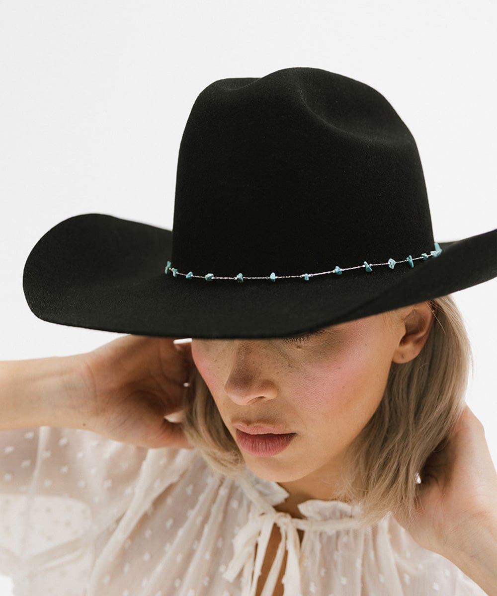 A woman wearing a black hat with a turquoise stone hat band around the base against a plain background #color_silver