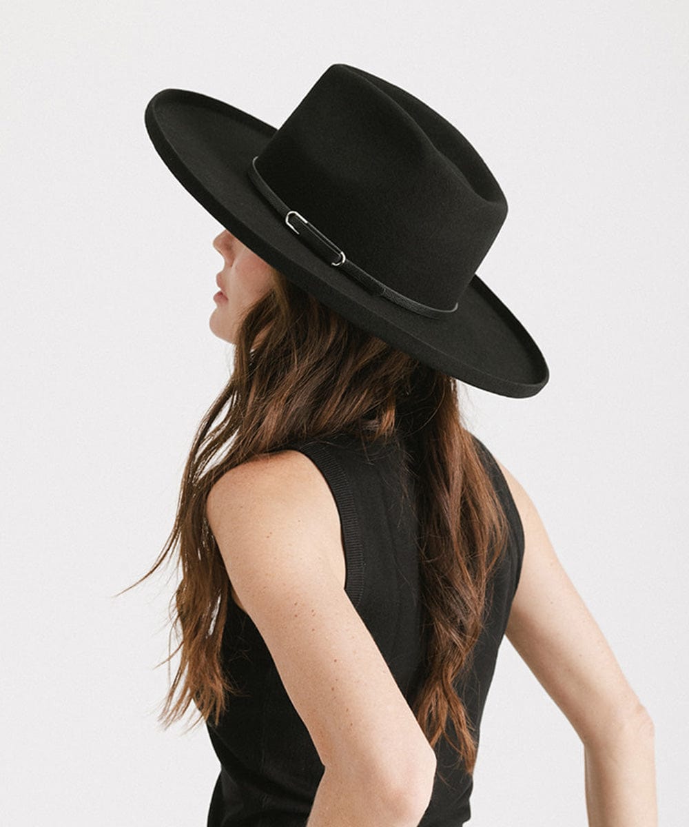 Woman wearing a black wide-brimmed hat with a black hat band and a black top, facing sideways against a plain background #color_black