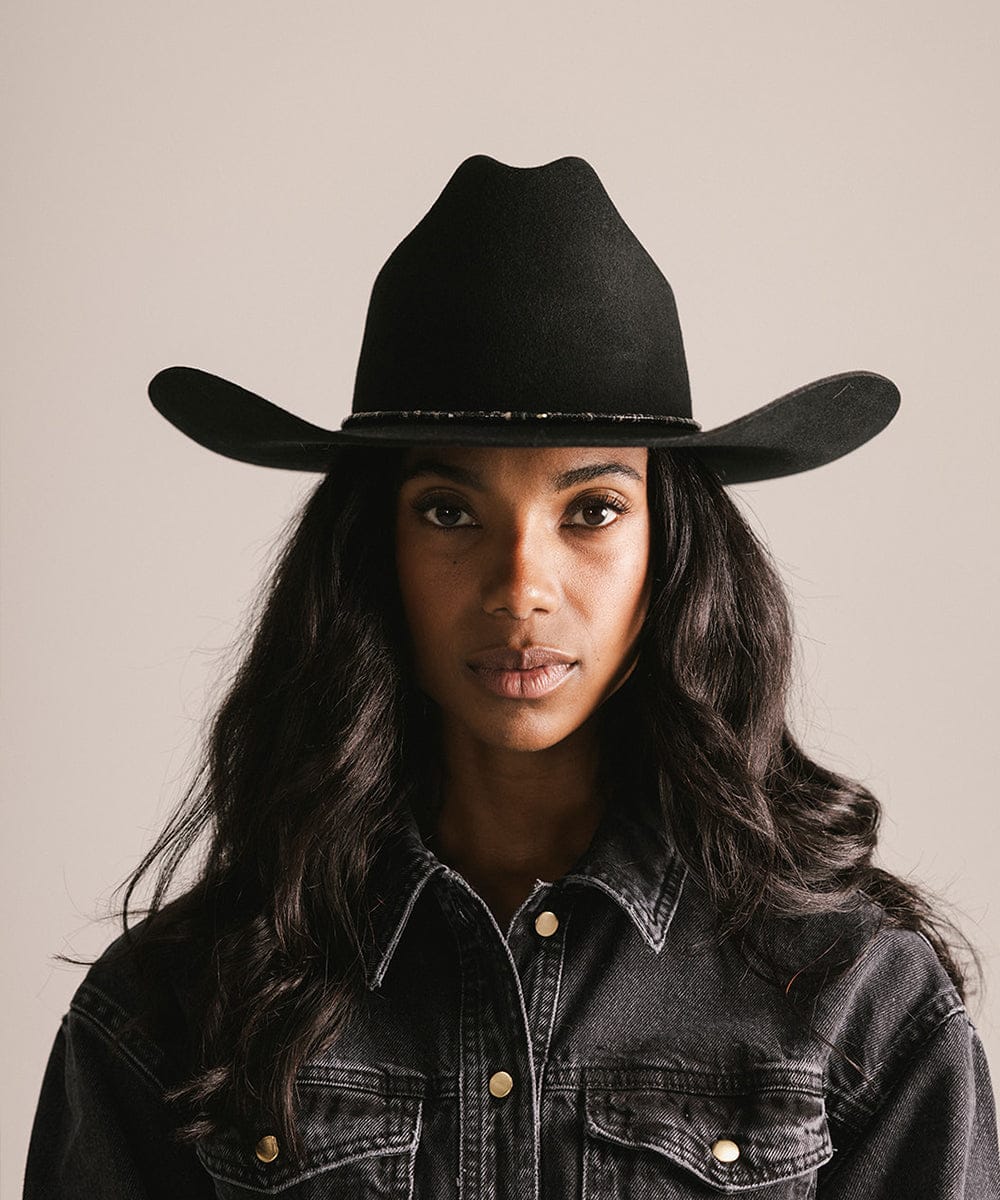 Woman wearing a black cowboy hat and denim jacket against a neutral background #color_black obsidian