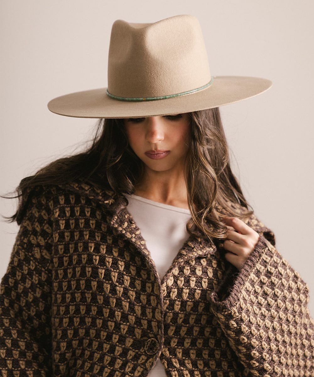 Woman wearing a beige hat and patterned coat against a neutral background #color_green jade