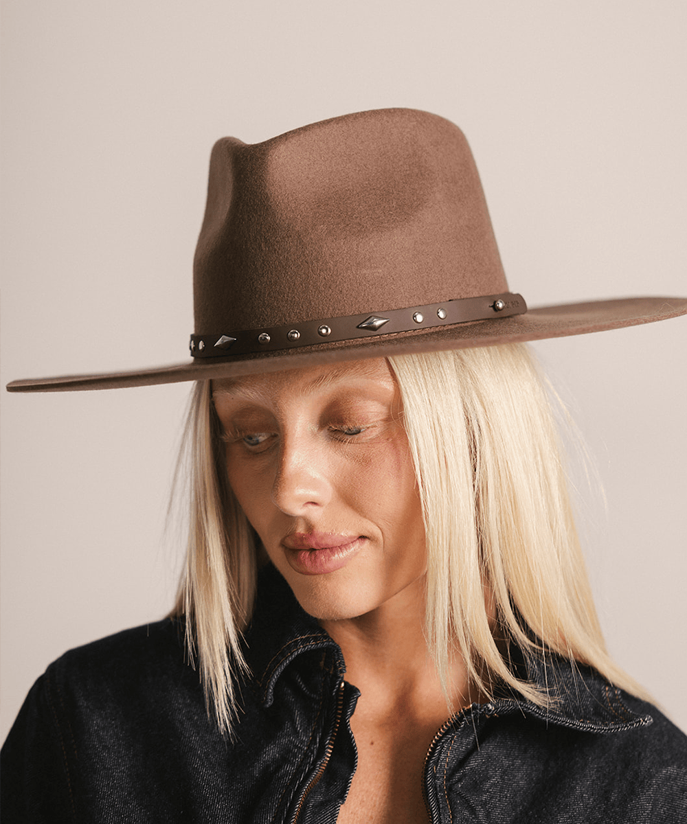 Woman wearing a brown hat with a chocolate colored studded leather hat band against a plain background #color_chocolate