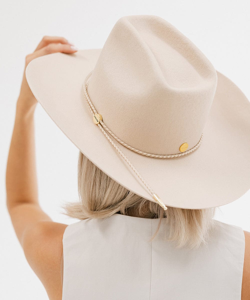 Woman wearing a cream cowboy hat with a cream braided hat band and a white top, facing behind against a plain background #color_cream