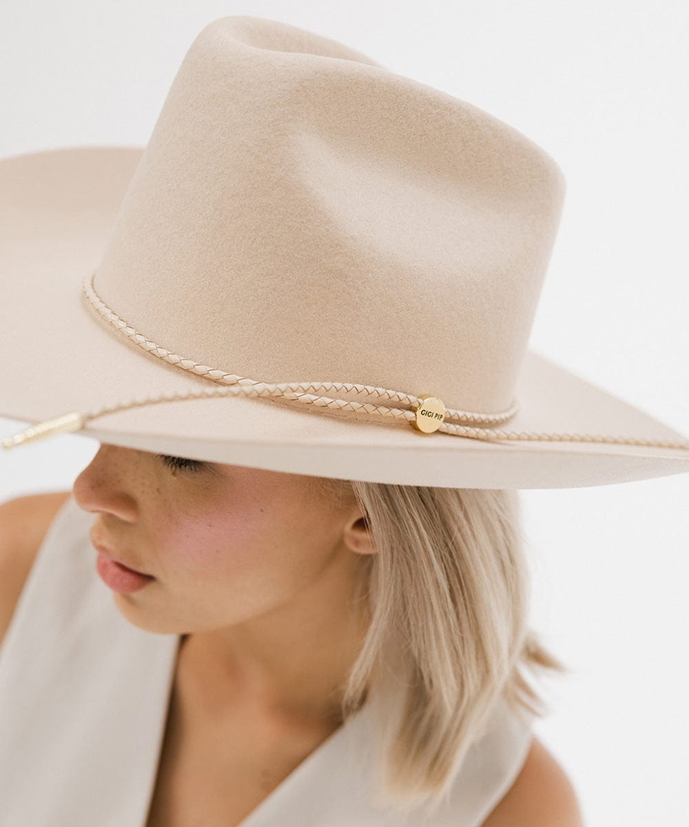 Woman wearing a cream cowboy hat with a cream braided hat band and a white top, facing sideways against a plain background #color_cream