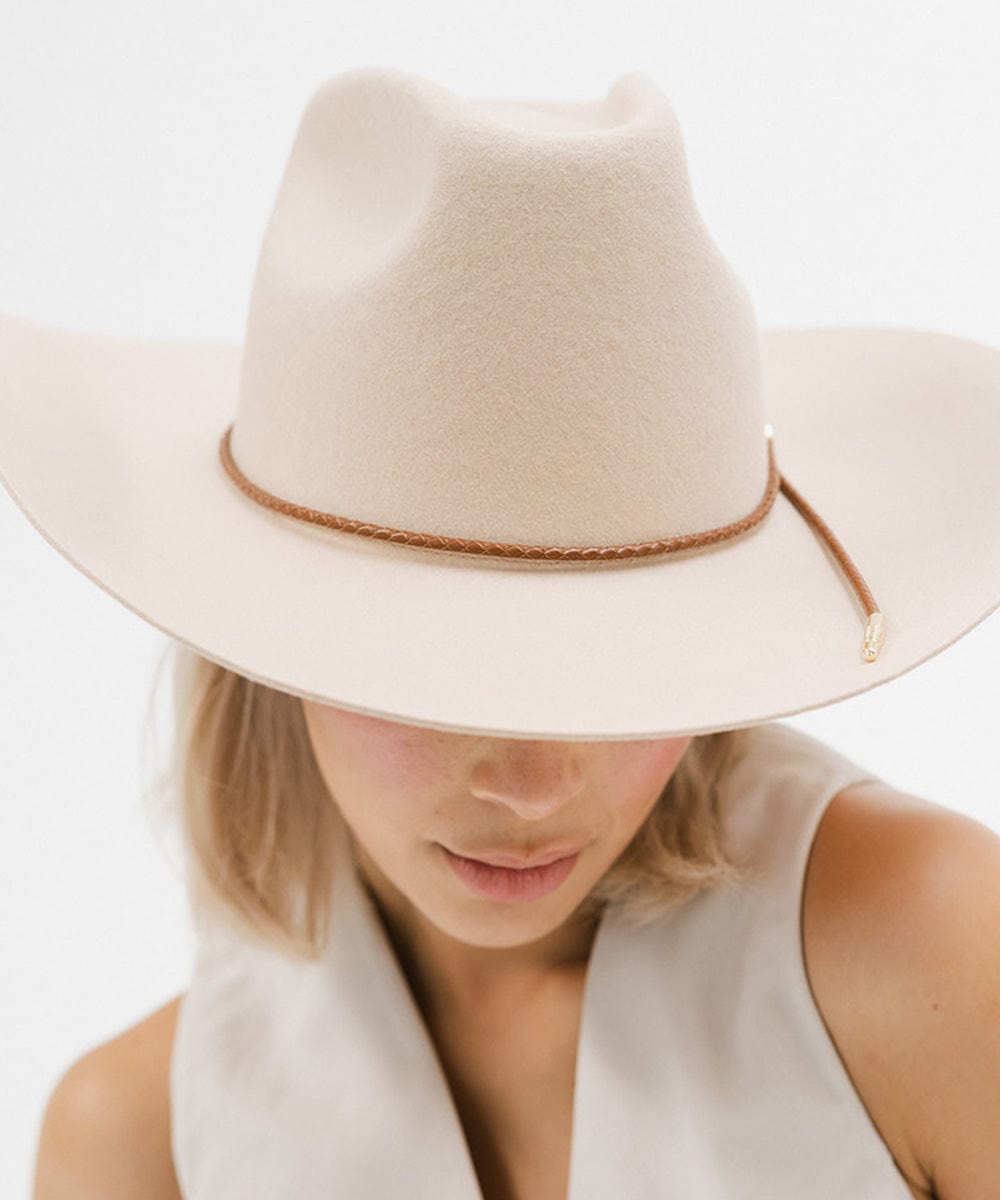 Woman wearing a cream cowboy hat with a cognac colored braided hat band and a white top against a plain background #color_cognac