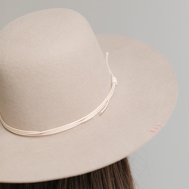 Close up image of a white cowboy hat with a cream hat band against a plain background #color_cream