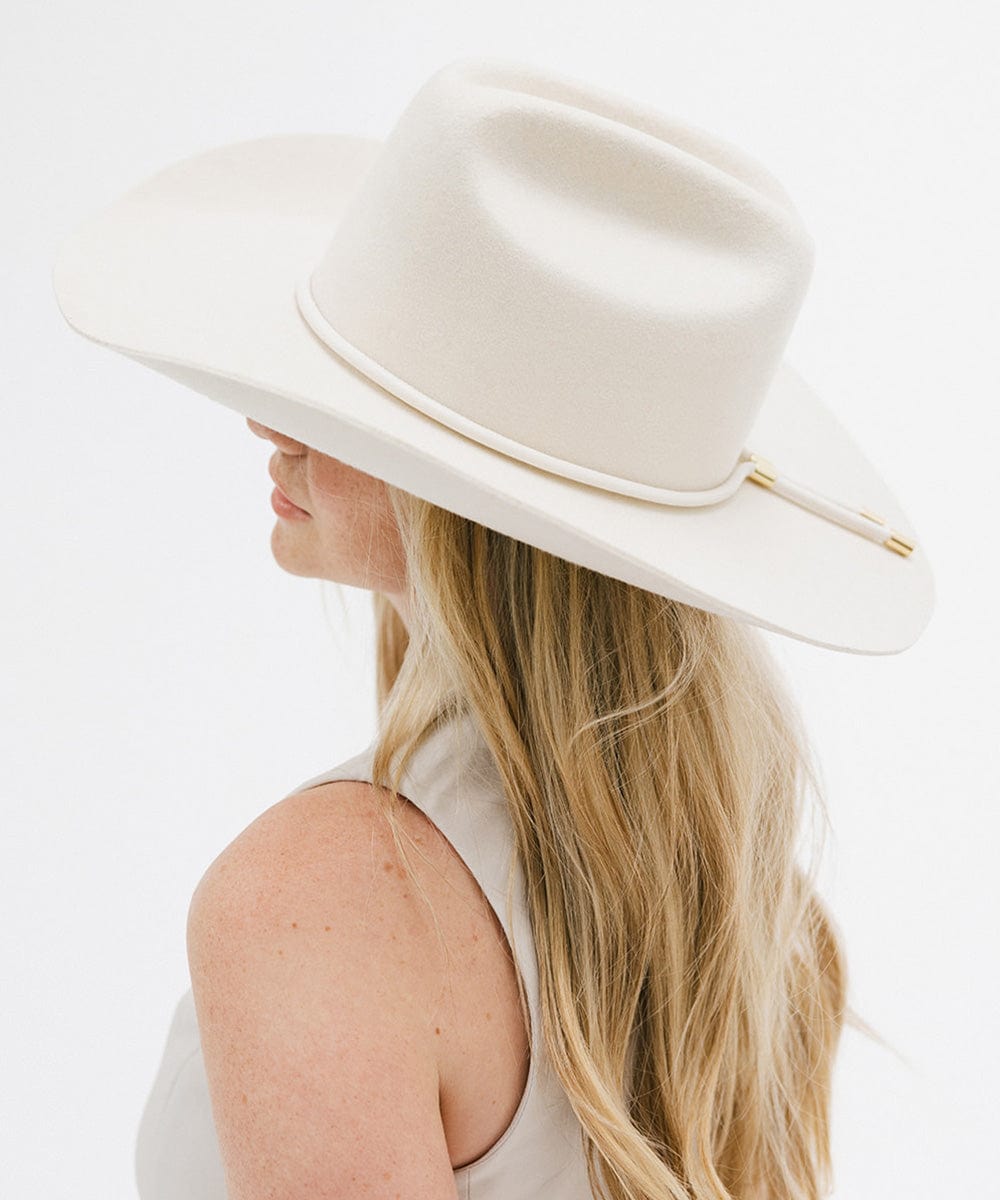 A person wearing a white hat with a vegan leather band featuring gold detailing. #color_off white