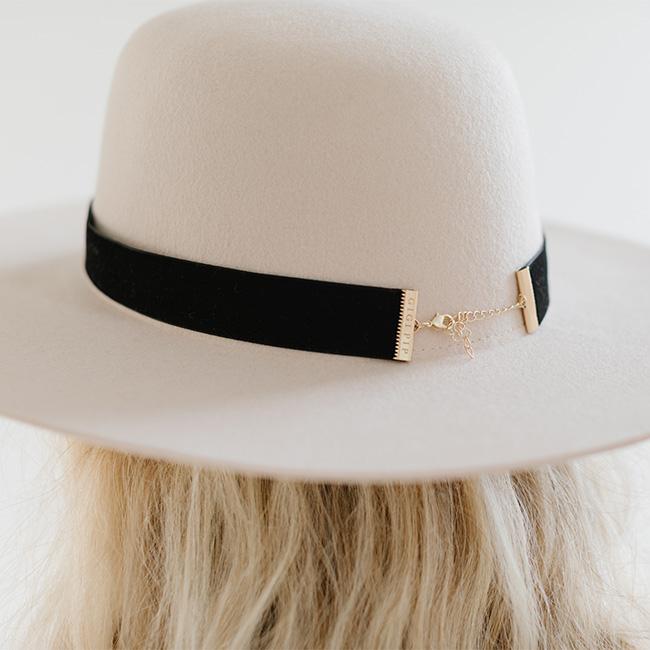 Close up image of a white hat with a black velvet chain hat band against a plain background #color_black