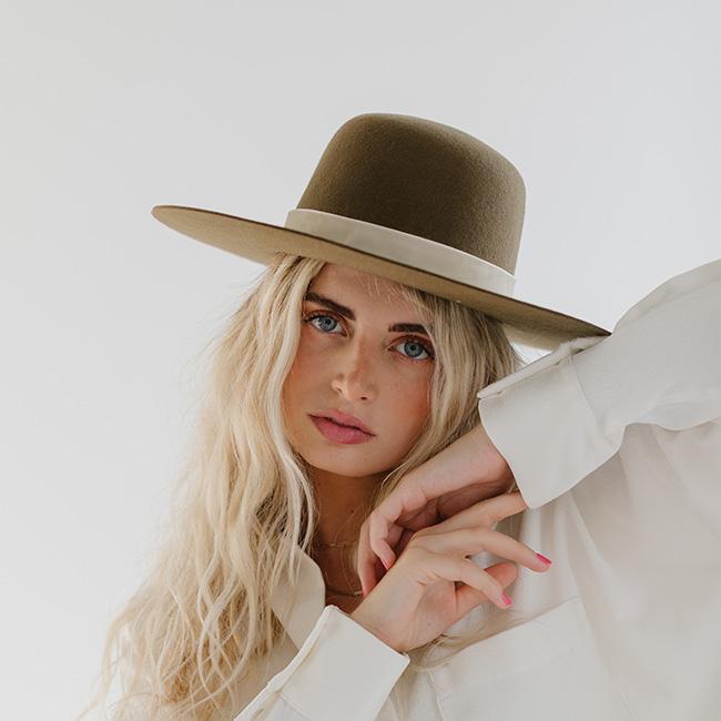 Woman wearing a brown hat with a cream velvet chain hat band and a white shirt against a plain background #color_cream