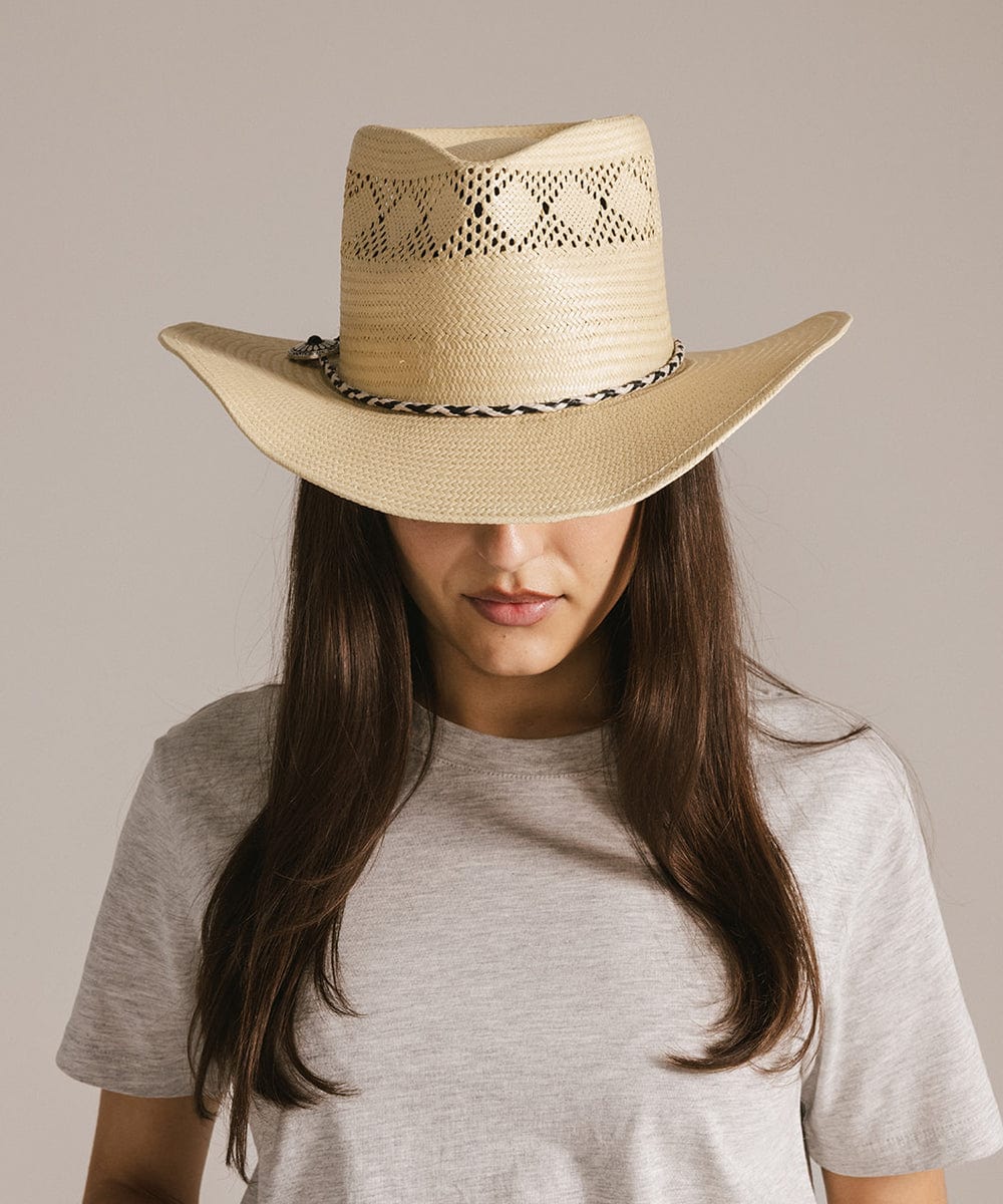 Woman wearing a beige hat with a black and white colored braided bolo tassel hat band and a grey t-shirt against a plain background #color_white-black