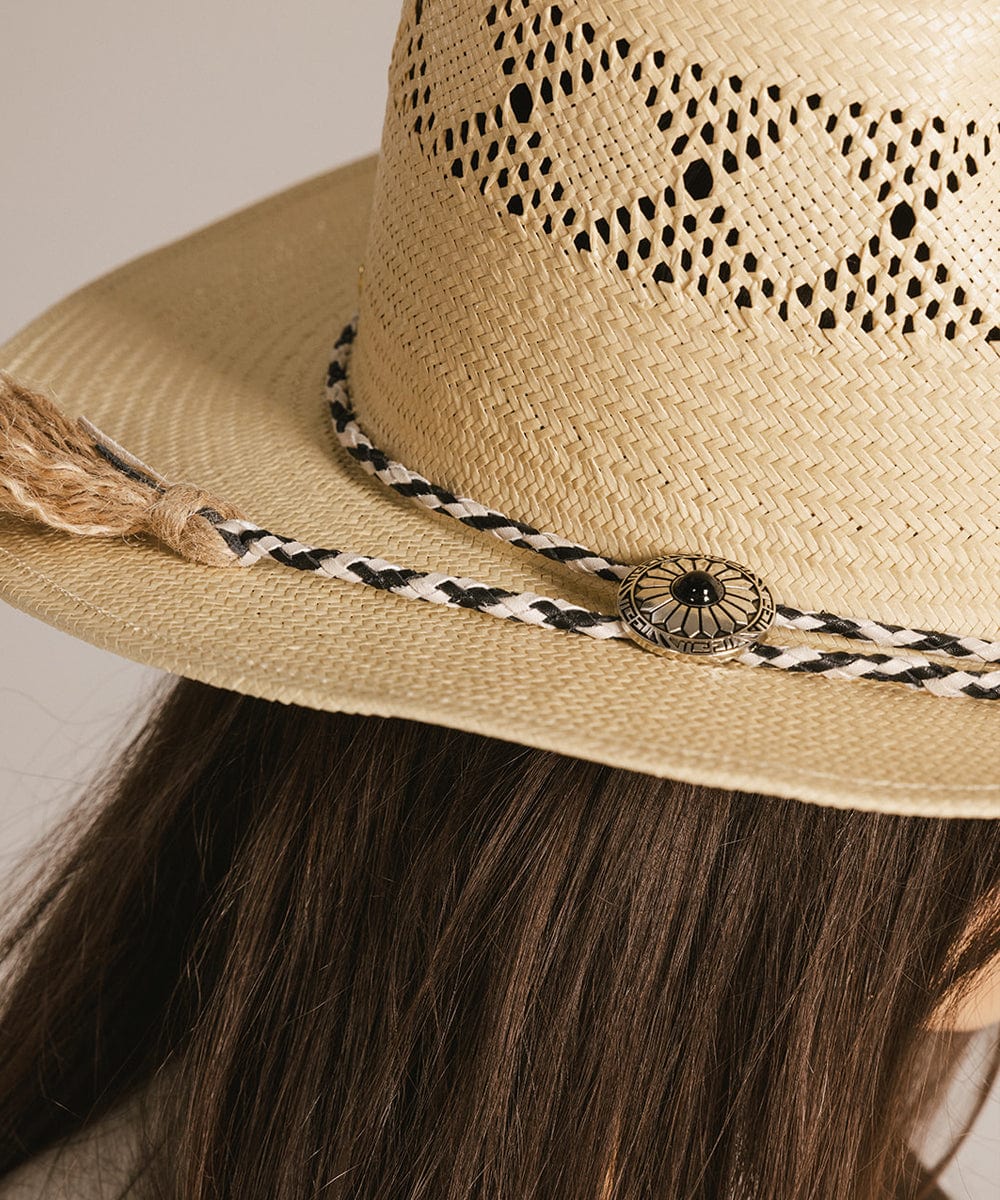 Close up image of someone wearing a beige hat with a black and white colored braided bolo tassel hat band against a plain background #color_white-black