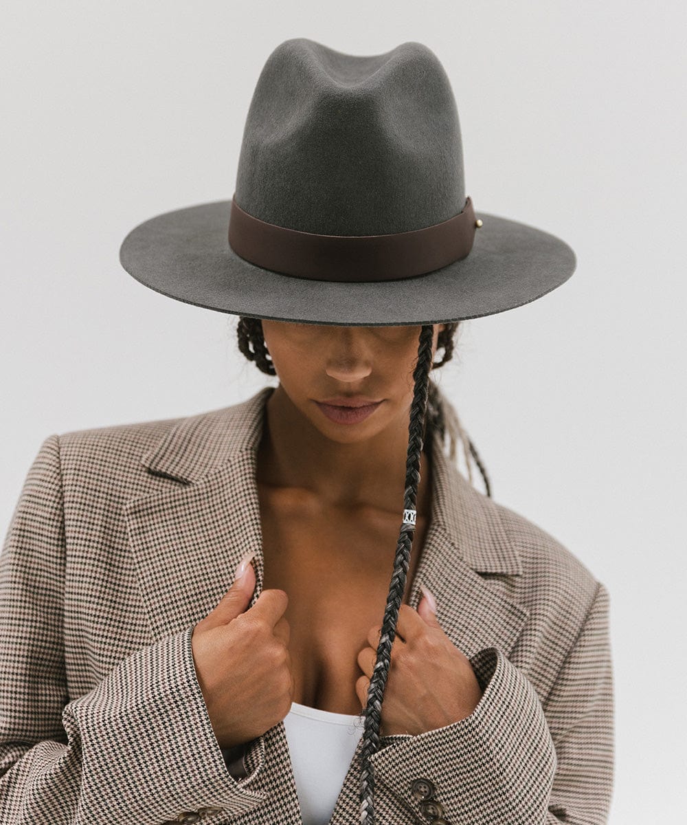 A woman wearing a grey hat with a wide chocolate colored leather band around the base, and a coat, posing against a plain background #color_chocolate