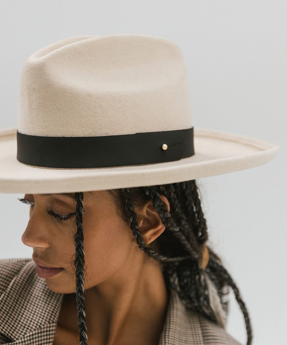 Woman wearing a cream hat with a wide black leather band around the base, facing sideways against a plain background #color_black