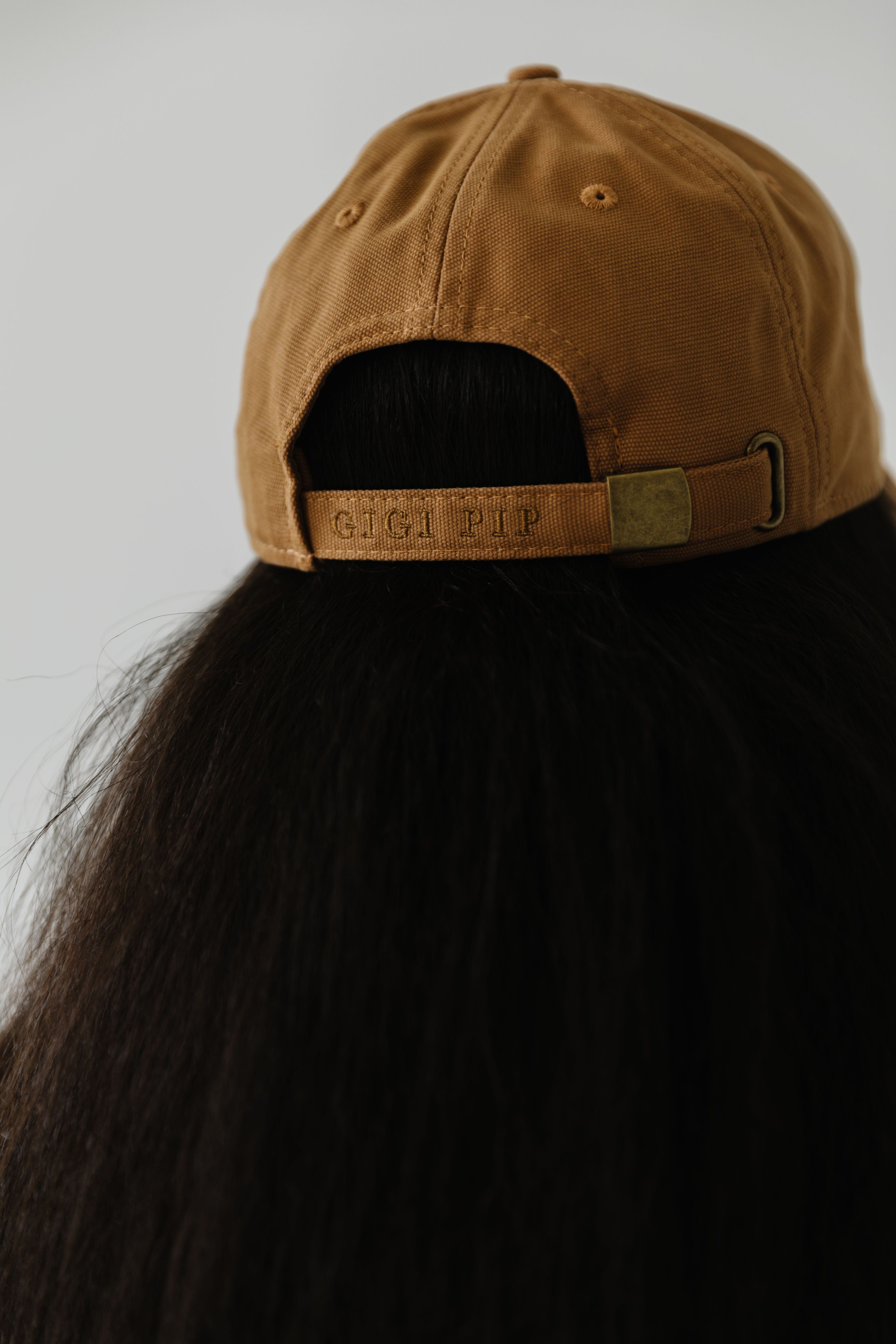 Woman wearing a camel colored ball cap facing behind against a plain background #color_camel