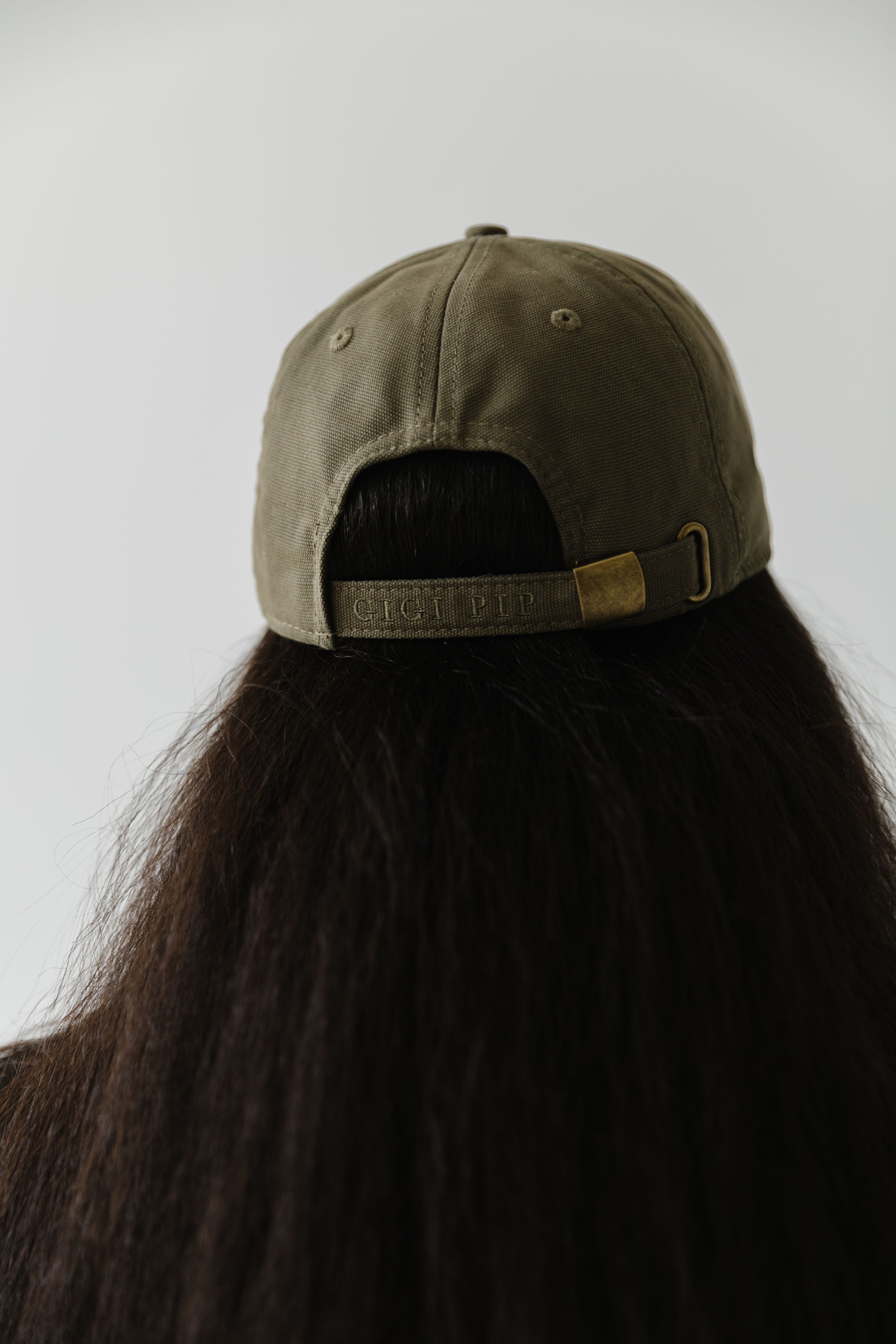 Woman wearing an olive colored ball cap facing behind against a plain background #color_olive