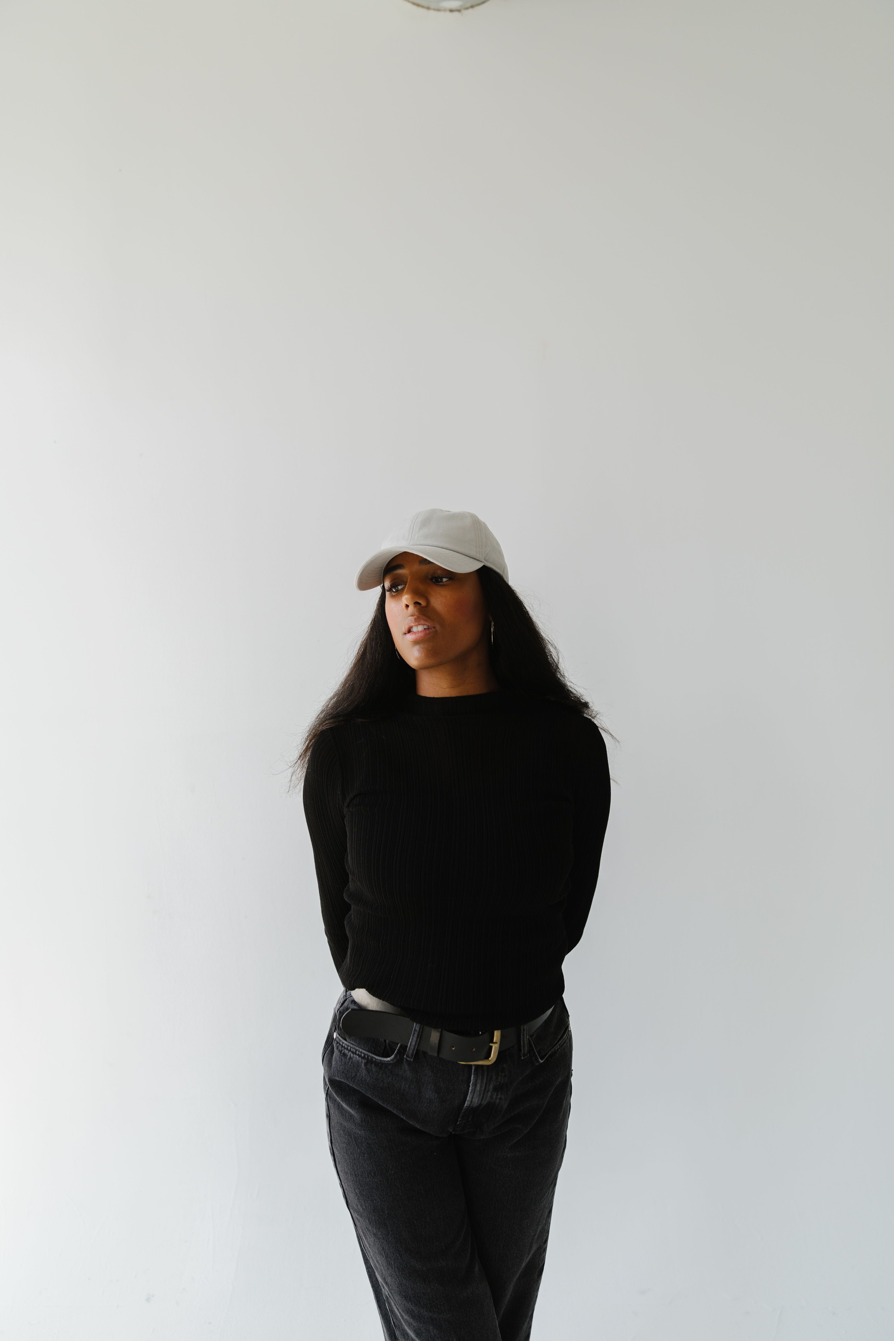 Woman wearing a stone colored ball cap, a black t-shirt and black jeans against a plain background #color_stone